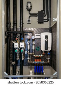 Water Pipes, Valves And Manometers Inside House, System With Electric Pumps And Heaters. Metal Pipeline Of Home Boiler, Cold And Hot Tubes On Utility Room Wall. Modern Pipe Installation For Heating.