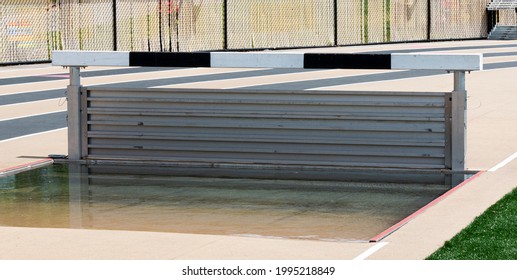 The Water Pit Of A Track And Field Steeplechase Is Full And Set At The Boys Height For A Race.