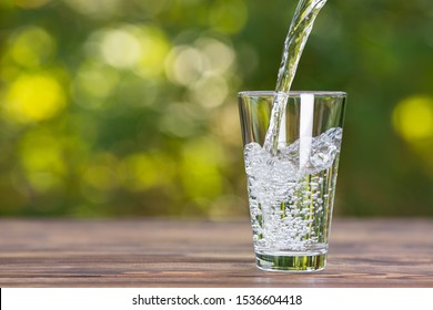 Water Pouring Into Glass On Wooden Table Outdoors