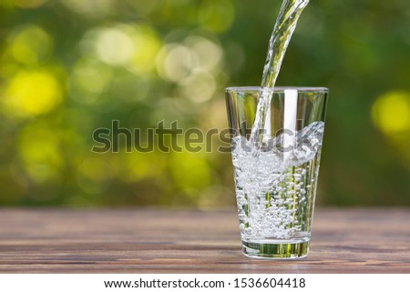 water pouring into glass on wooden table outdoors