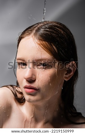 Water pouring on face of young model on abstract grey background 