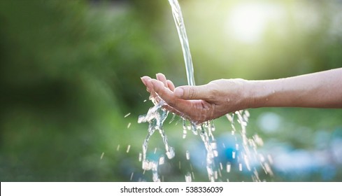 Water pouring in woman hand on nature background, environment issues