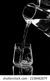 water pours into a glass from a decanter on black background.