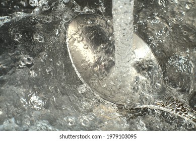 Water Pours On The Spoon In A Strong Stream And You Can See The Iridescent Drops In The Light. Closeup