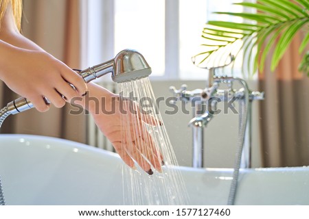 Water pours out of the shower on the girl's hands. On a blue background. Woman checks the temperature of the water in the background of the bathroom.