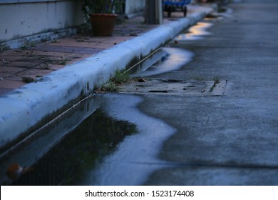 water puddle on the street. poor drainage system left water near catch basin drain inlet on a concrete road. narrow concrete blocks footpath too small for pedestrians