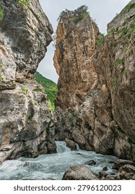 Water rapids flow between massive stone walls of a natural canyon. Steep rocky cliffs with hints of green foliage rise dramatically