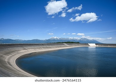 Water reservoir dam holding back water with mountains in background.