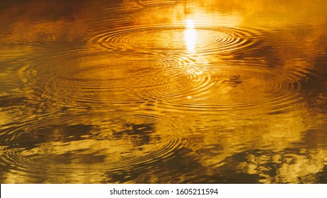 Water Ripple Circle On The Surface Of Lake Water With Reflection Of Sky Clouds At Sunset Or Evenig Time.