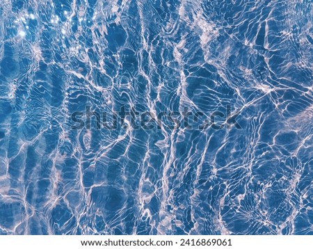 Water ripple over sandy beach. Transparent blue colored clear water surface texture with splashes. Water background, ripple and flow with waves. Blue water shinning. Sea, ocean surface.