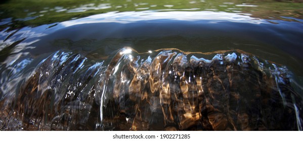 the water in the river flows down a large stone and shimmers in the sun - Shutterstock ID 1902271285
