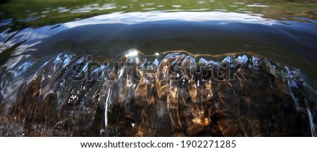 the water in the river flows down a large stone and shimmers in the sun