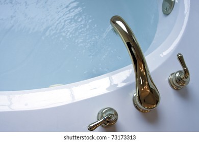 Water Running From Gold Plated Faucet Flowing Into A Garden Tub