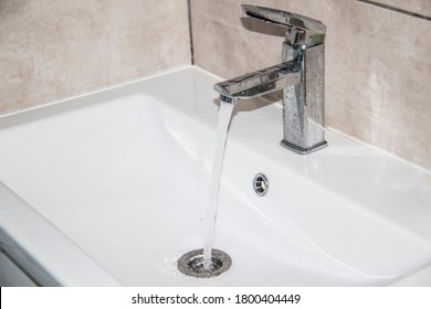 Water runs from the tap into the sink. Modern water tap in the bathroom with running flowing water in sink. Open chrome sink faucet. Modern design bathroom.