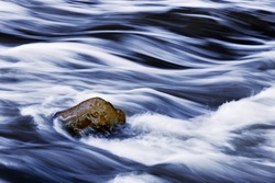 Water Rushing By A Rock In A River Forming A Smooth, Abstract, Painted Appearing Pattern.