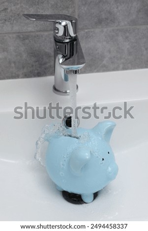 Water saving concept. Stream of water flowing from tap into piggy bank in bathroom
