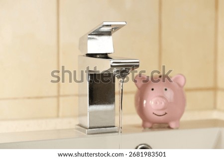 Water saving concept. Stream of water flowing from tap and piggy bank indoors, selective focus