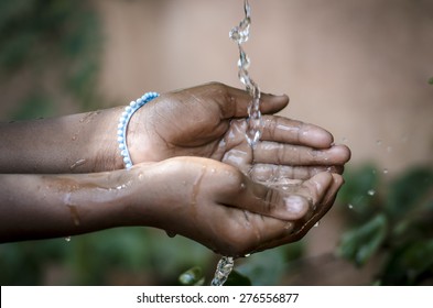 Water Spilling Into Black African Children's Hands (Drought / Water Scarcity symbol). Water scarcity is the lack of sufficient available water resources to meet the demands of water usage.