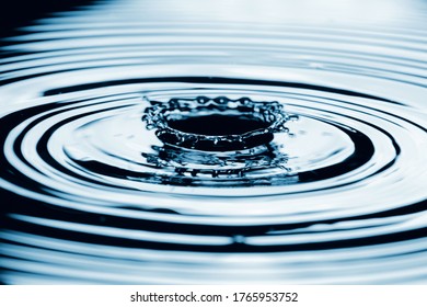 Water Splash In Dark Blue Color With A Drop Of Water Flying From Above.