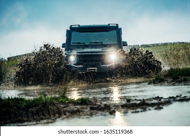Water splash in off-road racing. Classic 4x4 car crossing water with splashes on muddy road. Low angle view of front of SUV on mountain road