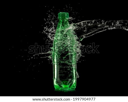 Water splash over a green sparkling water bottle on black background