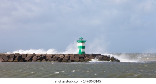 water splashes over lighthouse and pier near scheveningen harbor in the netherlands during summer storm