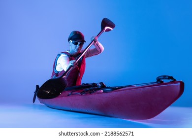 water sport activities. Sportive woman in red canoe, kayak with a life vest and a paddle isolated on blue background in neon light. Concept of sport, nature, travel, active lifestyle