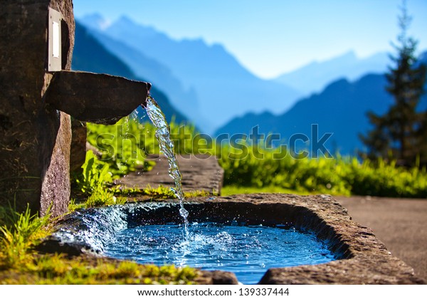 Water spring on Alps\
mountains background.