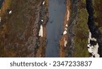 Water stream running between fields in iceland, aerial view of majestic oxarafoss cascade in icelandic landscape. Nordic waterfall running down off of frozen cliffs and hills. Slow motion.