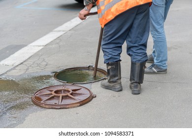 Water Supply Failure. From The Sewer Hatch, Water Flows. Workers Near An Open Hatch From Which Water Flows