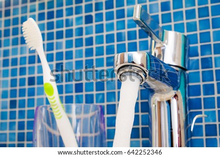 Water from tab in the bathroom with toothbrush in transparent glass