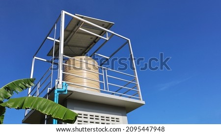 Water tank on the tower with solar panels. Close up water tank with solar panels on top for pumping soil in garden or farm water on blue sky background with copy space. Selective focus