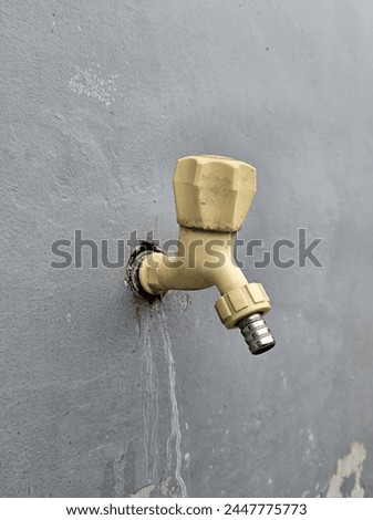 A water tap with a handle made of plastic, attached to a gray painted wall. 