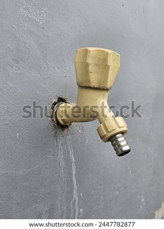 A water tap with a handle made of plastic, attached to a gray painted wall. 