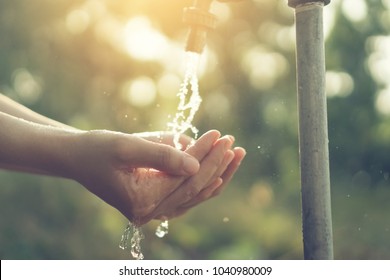 Water from tap to woman hand in nature green park and sunset sky with bokeh sun light abstract background. Environment and health care concept. Vintage tone filter effect color style.