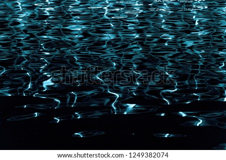 Water texture with color reflections on a black background. Blue glare from the windows reflected on the water surface of the pool. Black water with a neon glow. 