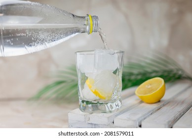 water or tonic is poured from a bottle into a glass with ice and lemon - Shutterstock ID 2081579011
