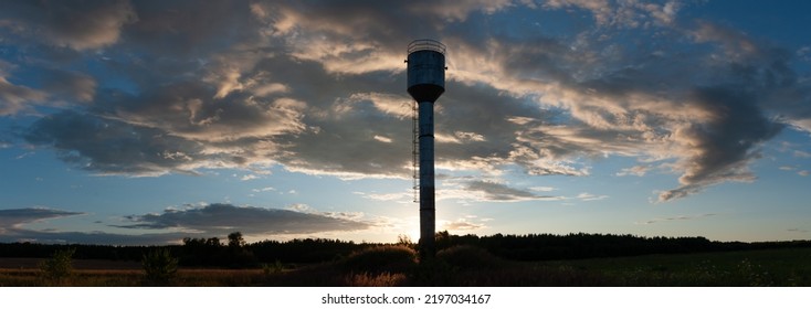 Water Tower Against The Backdrop Of Sunset And Clouds. Silhouette Image, Backlight