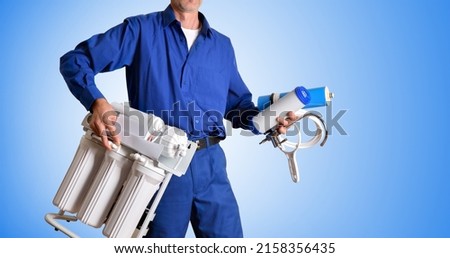 Water treatment technician with tools and spare parts for the maintenance and repair of reverse osmosis in the hands dressed in work clothes with blue gradient background. Front view.