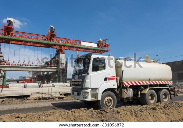 water truck running\
in the bridge construction site with gigantic steel machine\
operating in the\
background