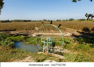 Water Turbine On A Cotton Field. Water Wheel And Channel For Watering Plants On The Field, Uzbekistan