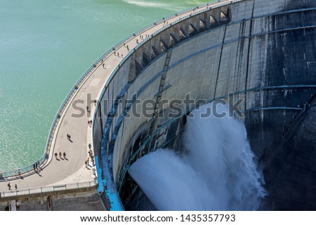 Water Turbines Are Producing Electricity At Power Plant. Panorama View Of Hydro Power Station And People On Kurobe Lake Dam,Toyama. River Dam and Tateyama Mountains.