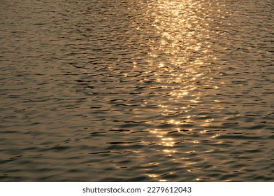 Water waves caused by wind. The sunlight that fell on the surface of the water turned golden. The reflected light looks glittering. - Shutterstock ID 2279612043