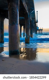 Water waves crash into concrete pillars under beach pier as the sun sets in background. Empty scenic outdoor location on a relaxing evening.