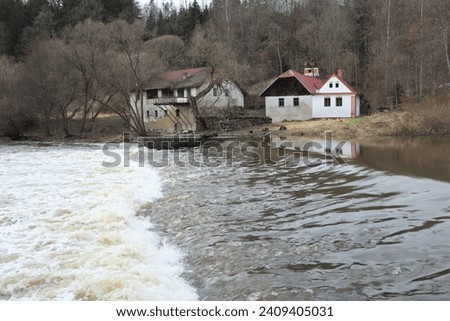 Water weir on Lužnice river close to Stádlec in the Czech Republic. Historical herritage - chain bridge is nearby. Old water mill is on opposite shore with spruce woods in background on steep hill.