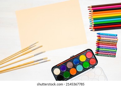 Watercolor oil paints, paintbrushes, colorful pencils, pastel crayons,blank watercolor paper pad. Creativity creation process. Artist's stuff on white table. Top view Flatlay of drawing supplies.