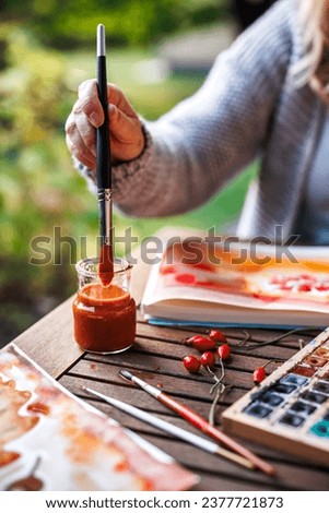 Watercolor painting. Woman artist is cleaning paintbrush in water and paints watercolor illustration outdoors
