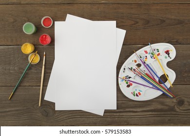 Watercolor Paints, Art Brushes, Easel And White Sheets Of Paper For Drawing On An Old Table