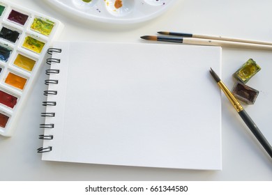 Watercolor paints, notepad and brushes, top view. Creative artistic mockup with copyspace