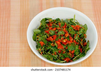 Watercress or cress with red bell pepper, carrot, ginger, lime juice, olive oil, salt and ground black peppercorn. Watercress and vegetable salad with homemade dressing in a round white bowl close-up